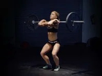 Atleta femenina en posición de recepción (squat) de una cargada olímpica, variante de recepción del levantamiento para entrenar desaceleración de carga y mejora del aterrizaje